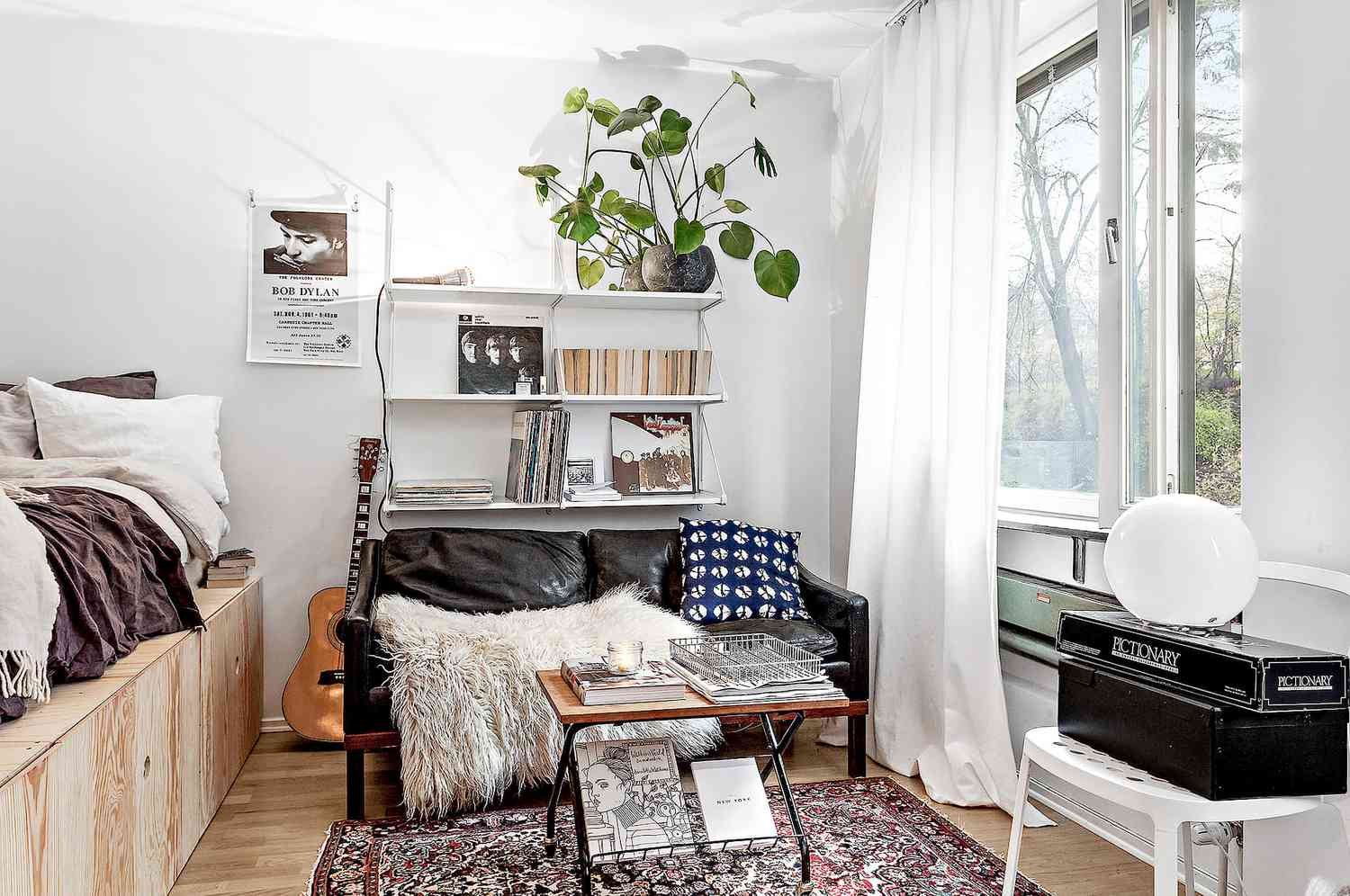 Cama de plataforma de contrachapado en apartamento estudio con librería, sofá de cuero y mesa de centro.