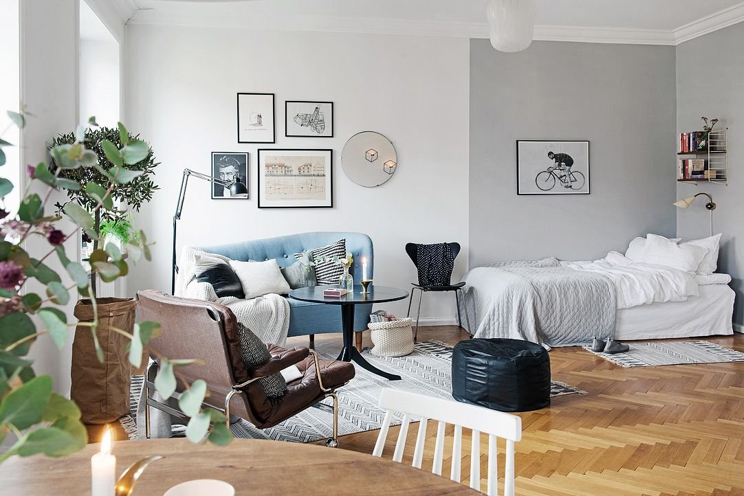 Pared de galería en un apartamento estudio con cama, sofá azul y mesa de cristal.