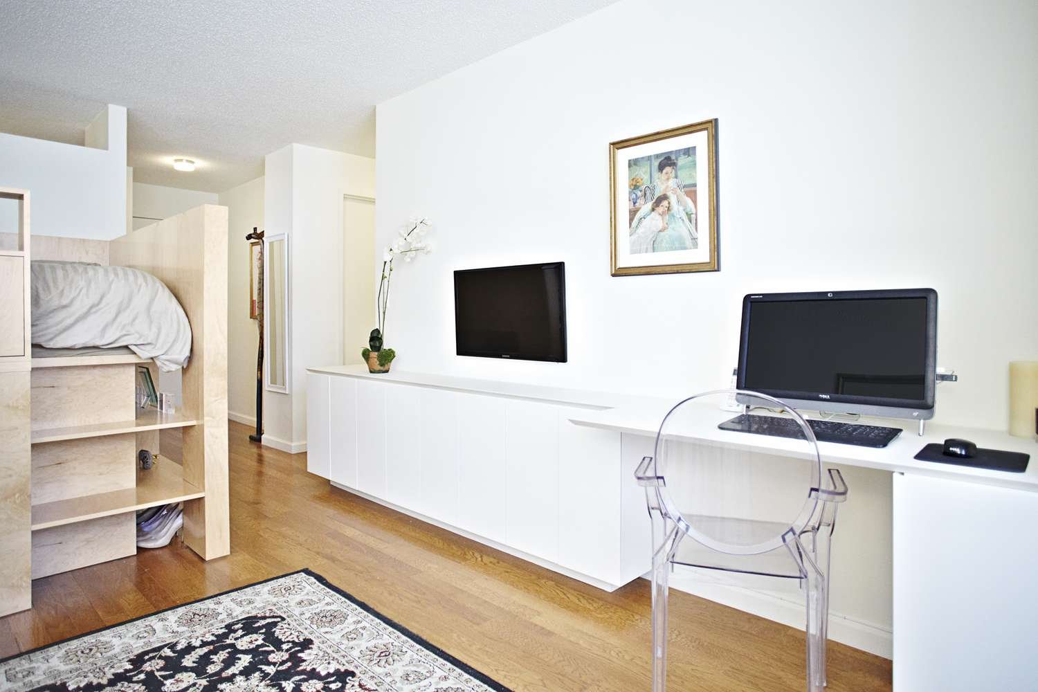 Cubby a medida para la cama en un apartamento estudio con televisión y ordenador sobre el escritorio.