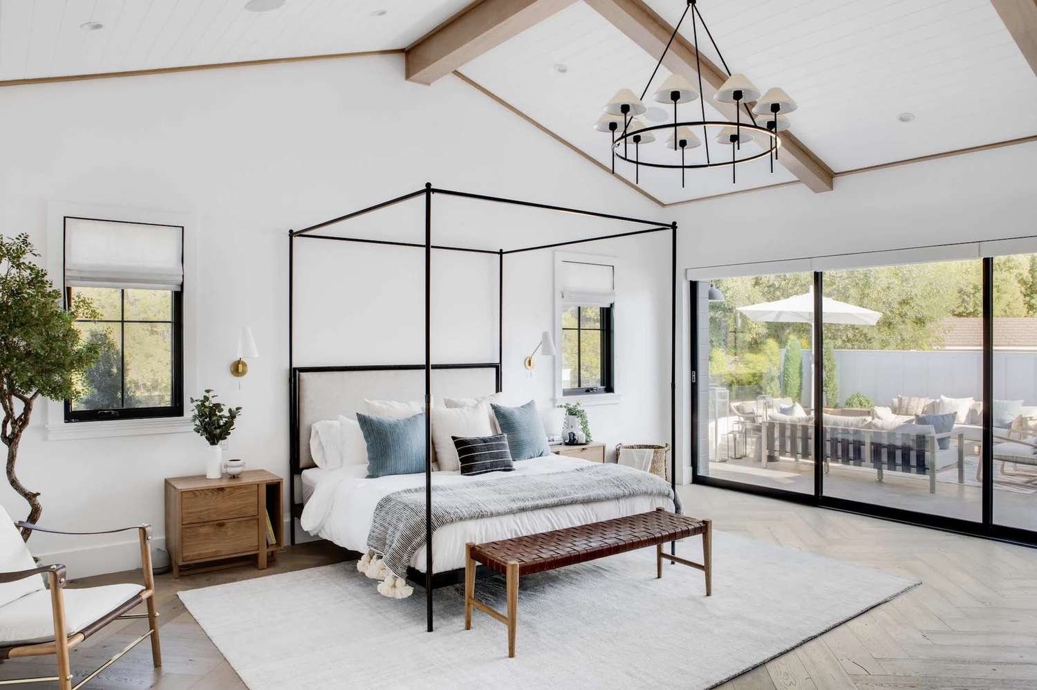 dormitorio moderno con somier de cuatro postes de metal negro, arbol bonsai, mucha luz natural
