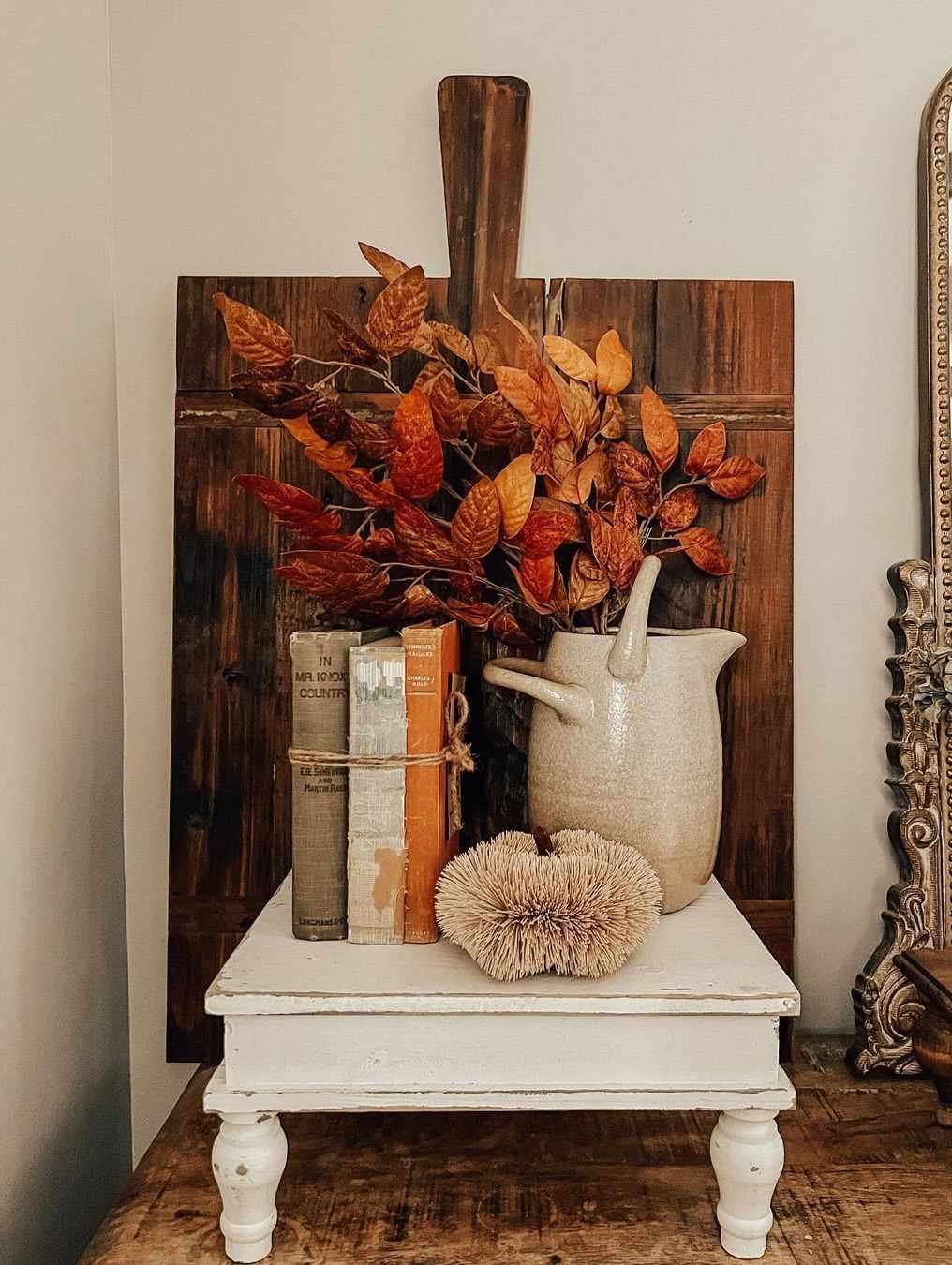 Una pequeña mesa cubierta de hojas otoñales, una pila de libros y una calabaza de paja.