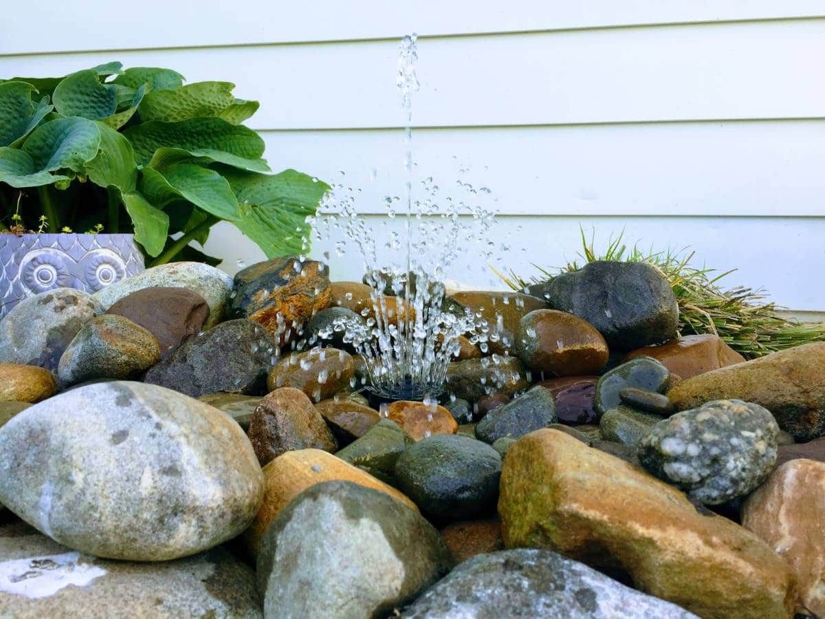 Agua saliendo rociada por debajo de rocas de río mojadas.