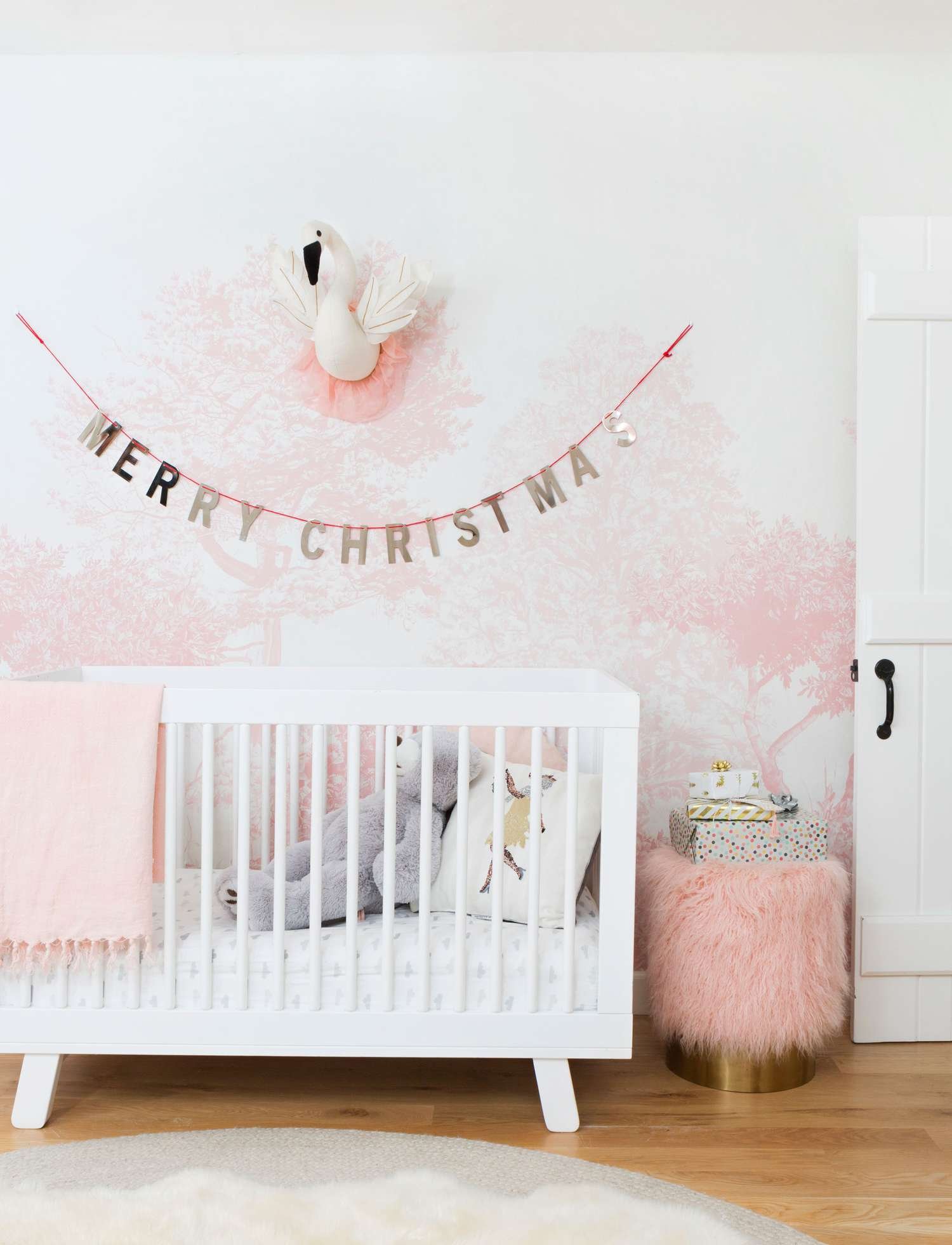 Cartel de Feliz Navidad colgado encima de una cuna en un cuarto infantil rosa y blanco