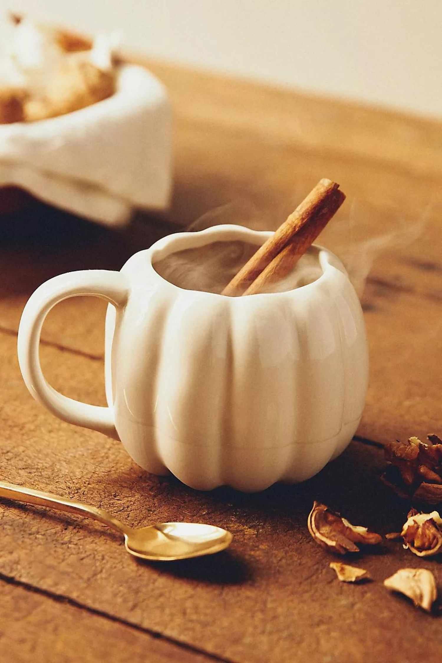 Una taza de cerámica blanca en forma de calabaza con una bebida caliente y una rama de canela