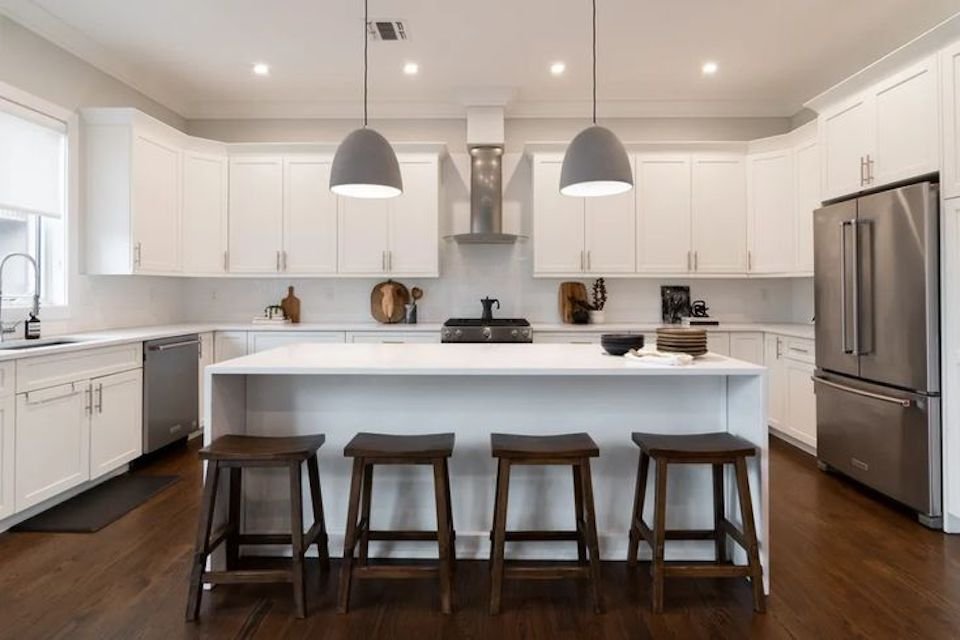 Cocina totalmente blanca con suelos de madera oscura y electrodomésticos de acero inoxidable