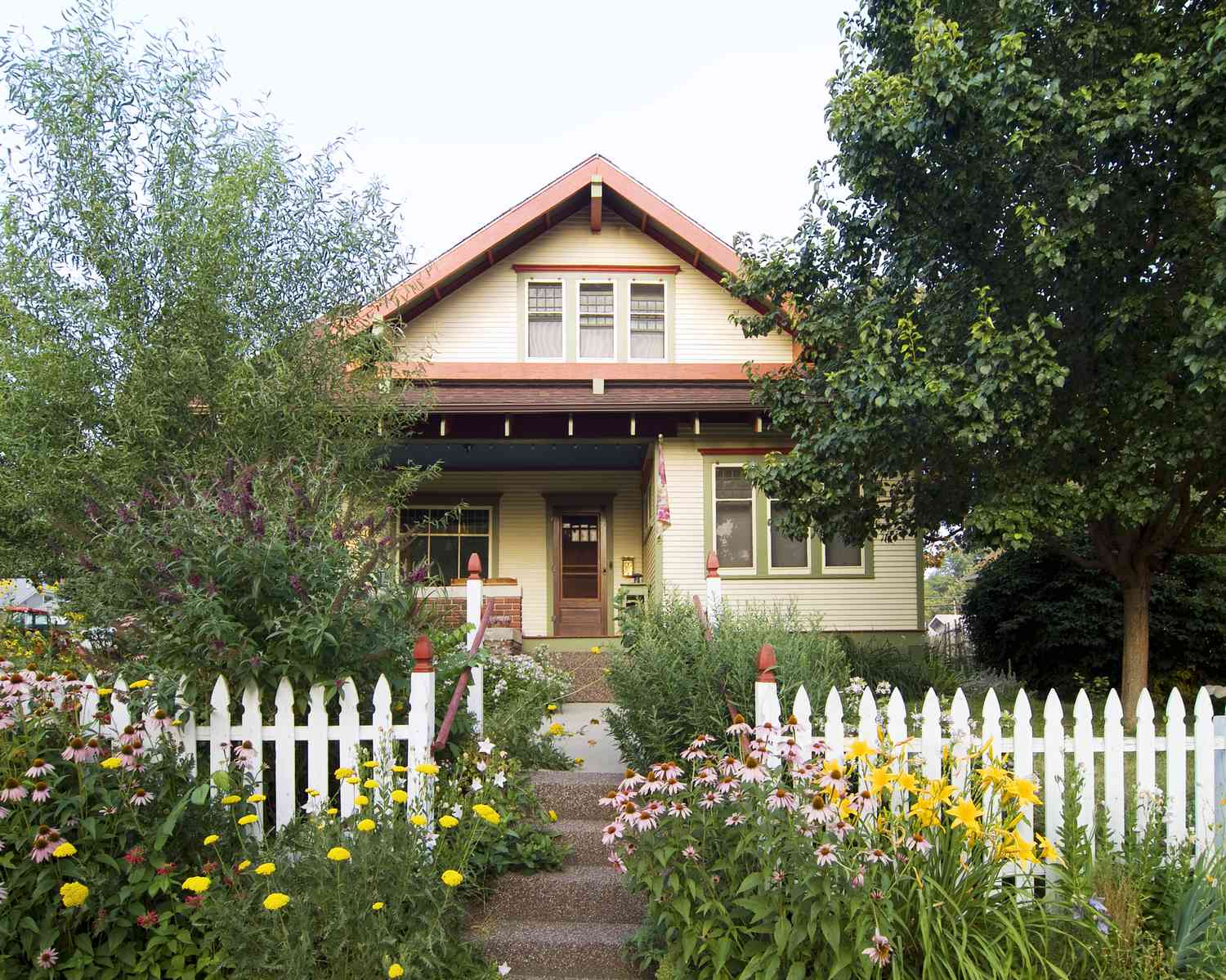 Casa bungalow salmón, exterior beige y verde con valla de piquetes blancos