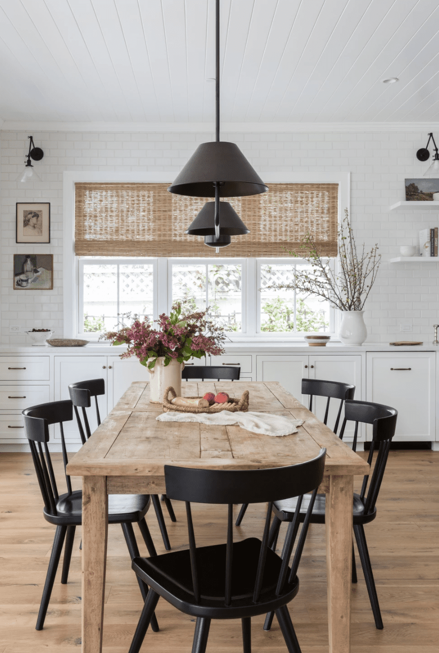 Una mesa de comedor rústica, decorada con un jarrón lleno de flores y una bandeja con pan y fruta