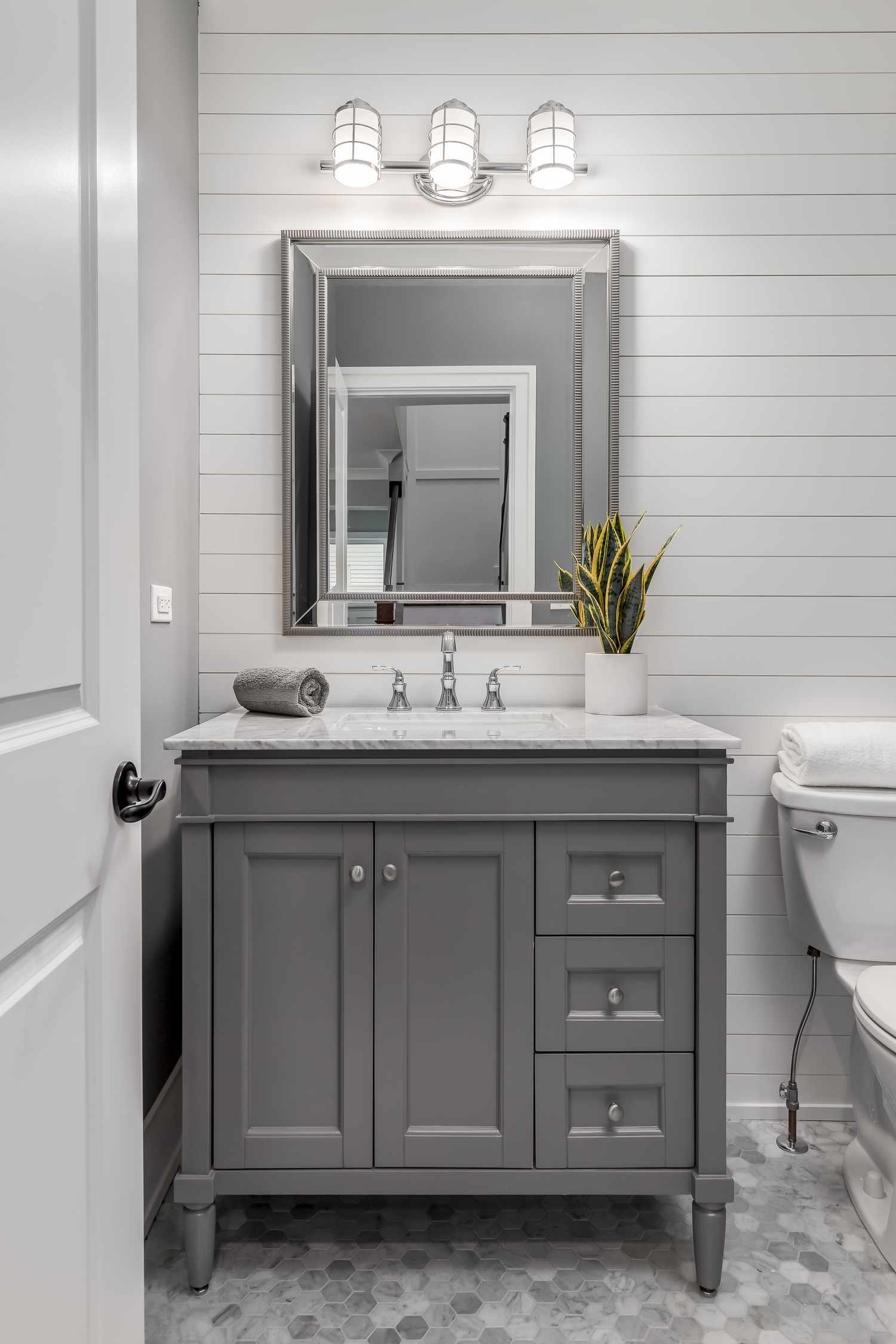 cuarto de baño gris con lavabo oscuro, paredes de shiplap y suelo de guijarros