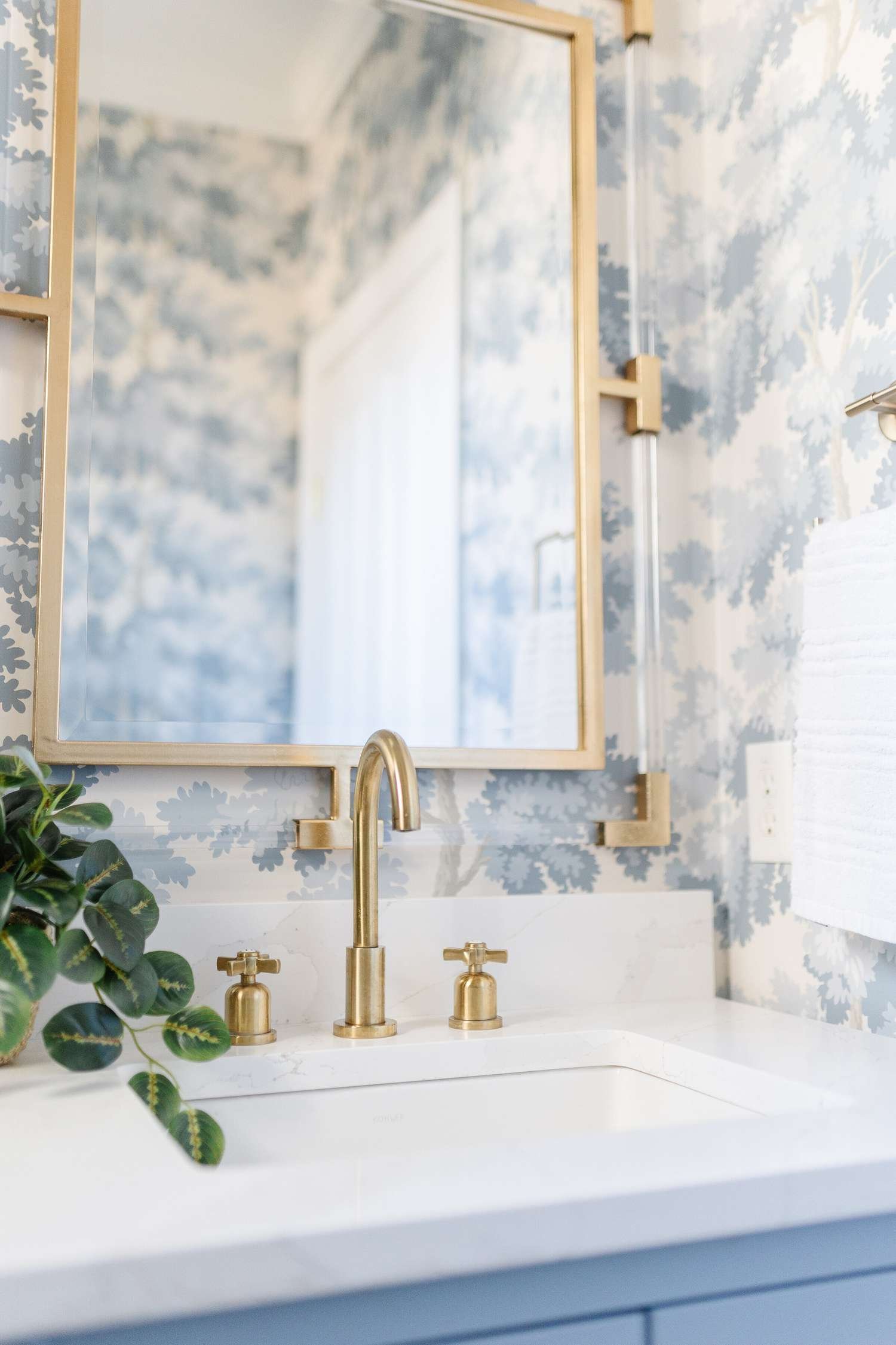 Cuarto de baño con papel pintado azul claro y blanco y detalles en latón